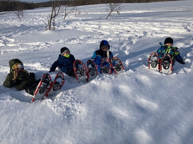 students laying in the snow with snowshoes